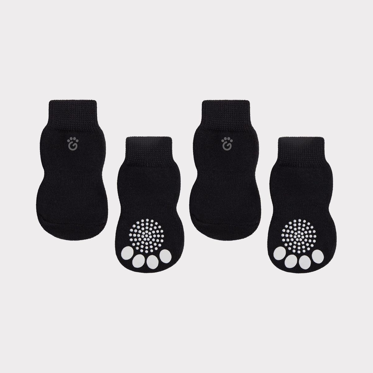 Four black pet socks arranged in a row on a light gray background. Two socks show the top view with a small paw print logo near the cuff, and two show the bottom view with white paw pad grip pads on the sole.