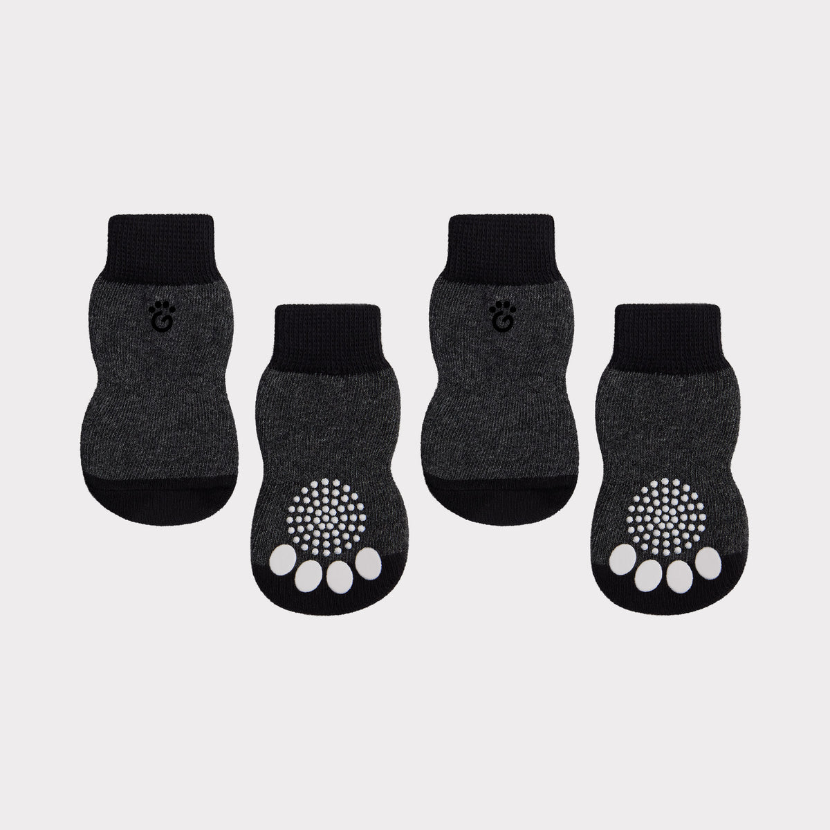Four dark gray and black pet socks arranged on a light gray background, with two socks showing a white paw-print grip pattern on the sole and a small paw-print logo on the cuff.